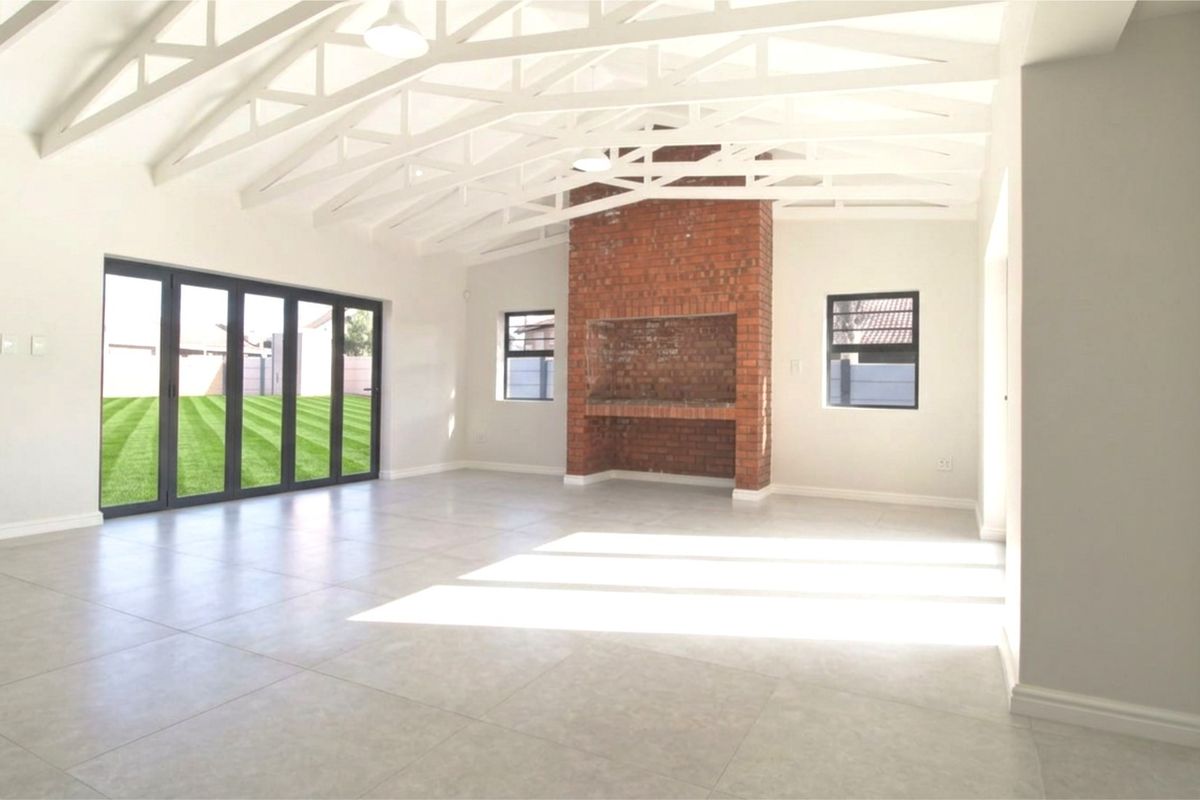 Spacious open-plan living area featuring exposed white timber trusses, a central brick fireplace, large tiled floors, and expansive stacker doors leading to the garden.