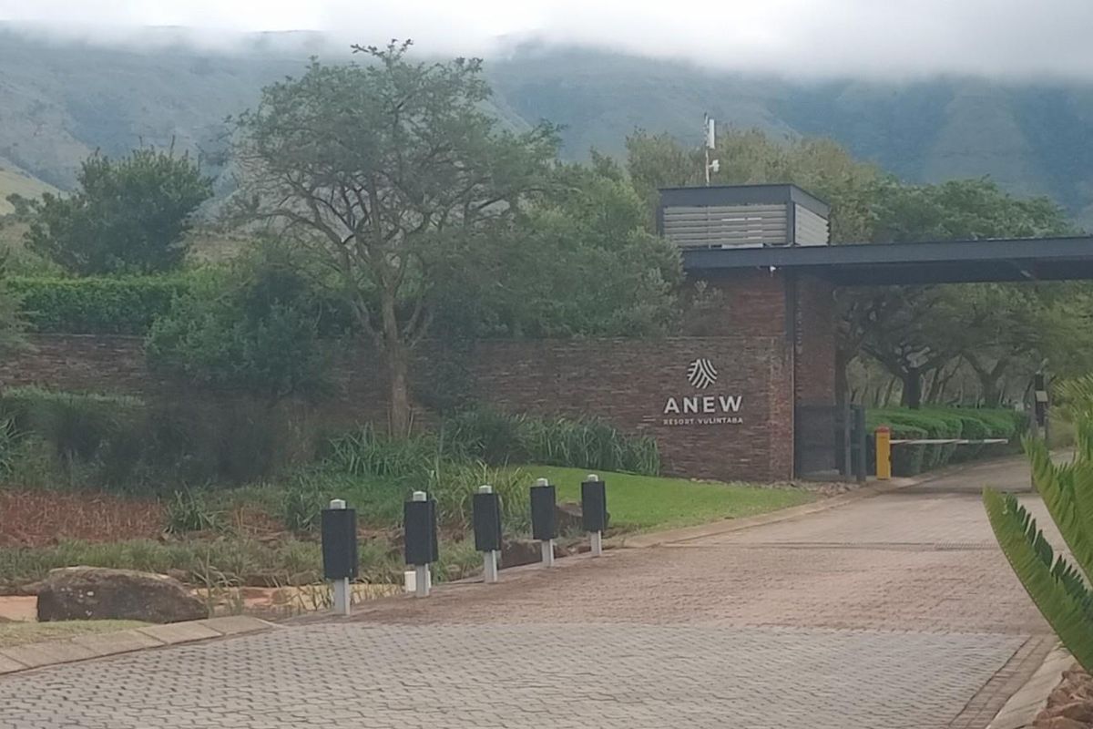 Entrance view of the residential estate featuring a paved driveway, stone boundary wall, and landscaped surroundings with mountain views.