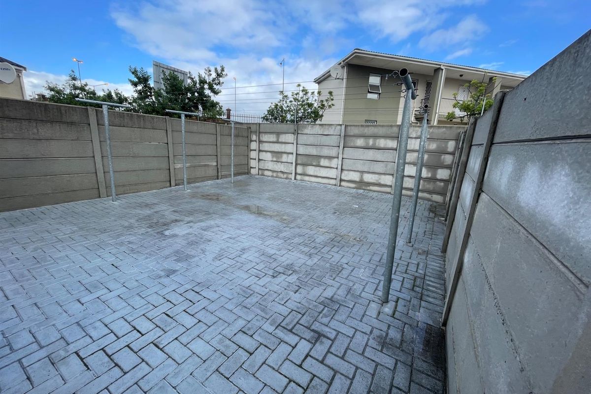 A private, paved rear courtyard enclosed by precast concrete boundary walls, featuring fixed metal washing line poles.