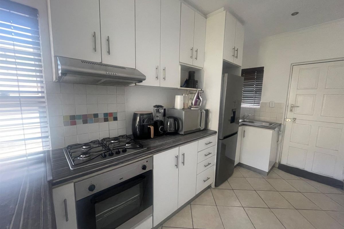 Functional kitchen featuring white cabinetry, dark laminate countertops, gas hob, built-in oven, extractor fan, and tiled flooring with a separate sink area.