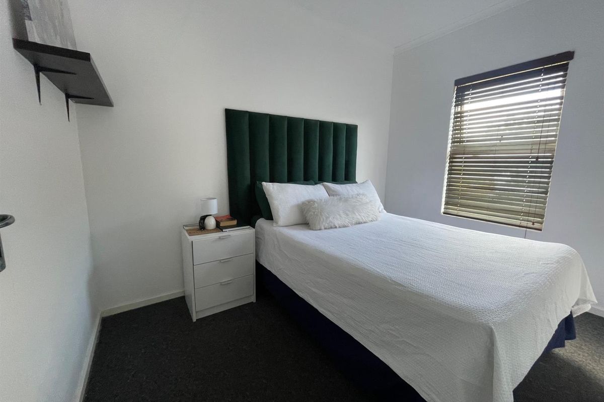 A well-maintained bedroom featuring neutral walls, dark carpet flooring, and venetian blinds for adjustable natural light.
