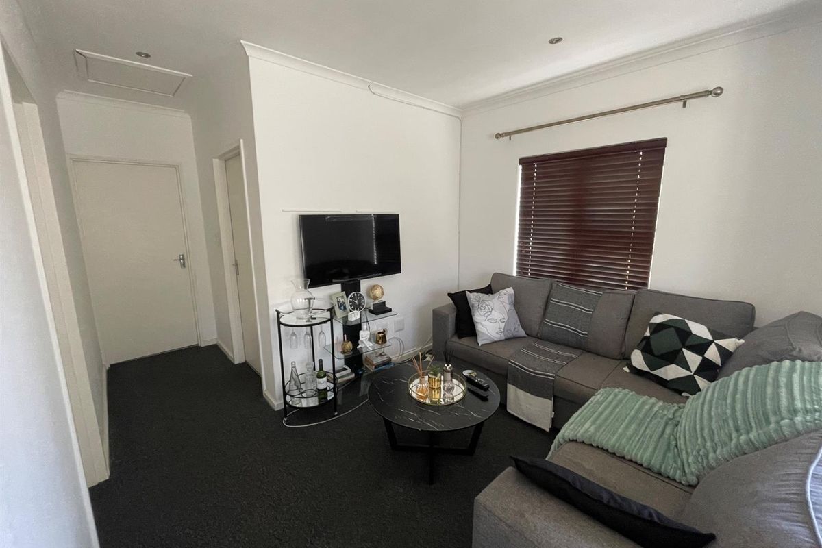 A comfortable living room featuring dark carpeting, recessed downlighting, and venetian blinds, providing a neutral and functional space.