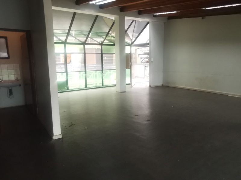 Open plan commercial office space featuring exposed timber beams, a small kitchenette area, and large glass atrium windows providing natural light.