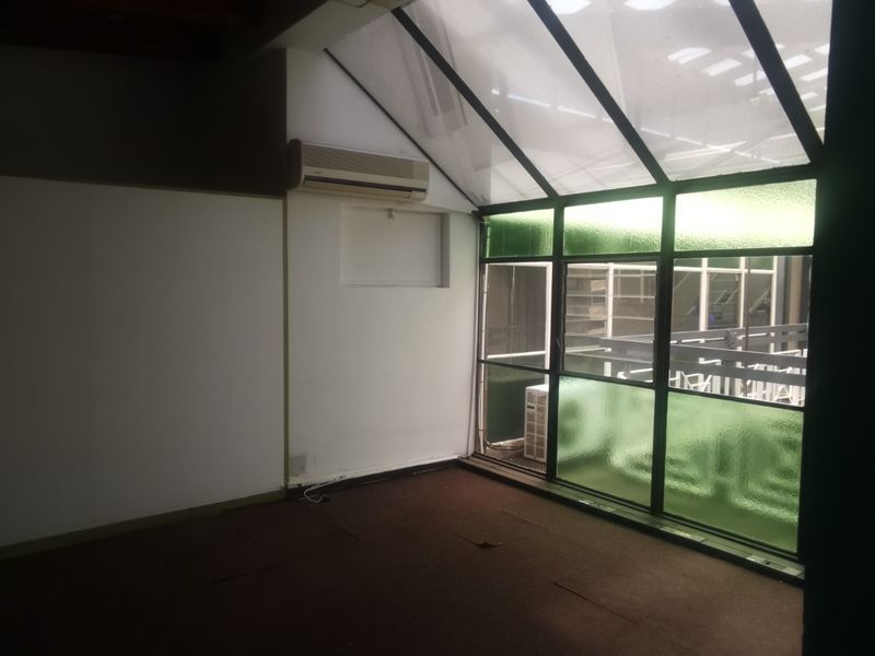 Empty office space featuring a sloped glass roof, aluminium window frames, wall-mounted air conditioning unit, and carpeted flooring.
