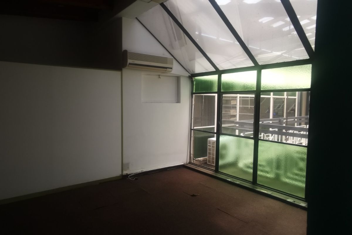 Empty office space featuring a sloped glass roof, aluminium window frames, wall-mounted air conditioning unit, and carpeted flooring.