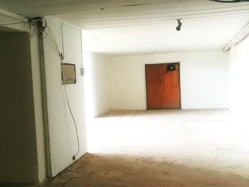 An empty, open-plan commercial space featuring exposed ceiling beams, concrete flooring, and a set of wooden double doors.