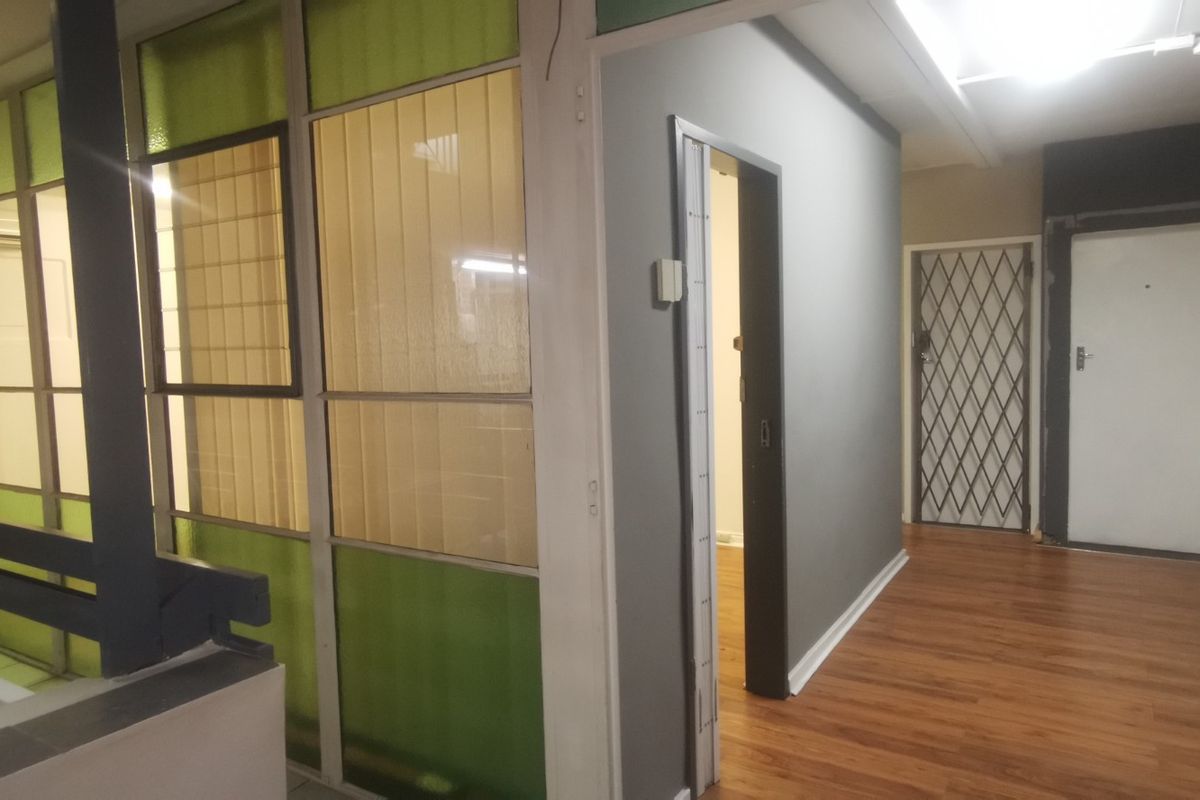 A commercial hallway featuring laminate flooring, a glass partition wall, and secure access doors.