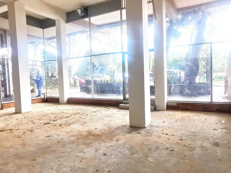 Spacious commercial interior featuring floor-to-ceiling glass windows, concrete flooring, and structural pillars, offering an open-plan layout suitable for various business configurations.