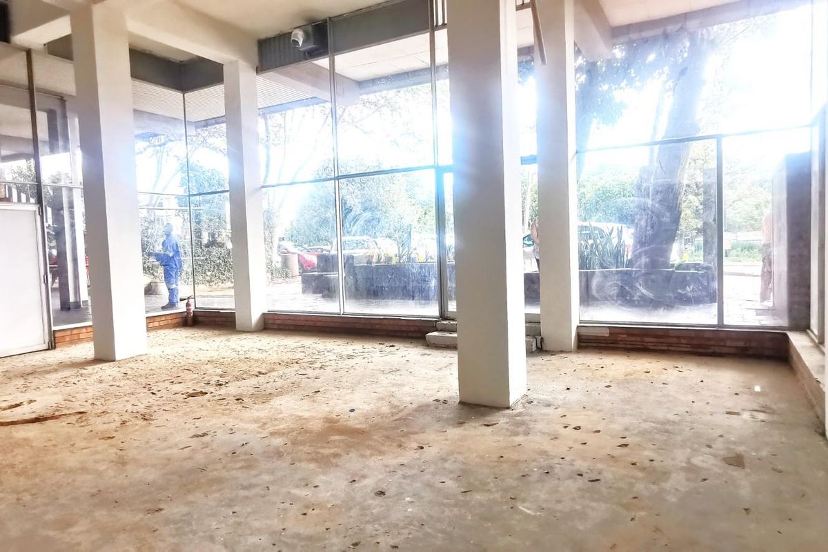Spacious commercial interior featuring floor-to-ceiling glass windows, concrete flooring, and structural pillars, offering an open-plan layout suitable for various business configurations.