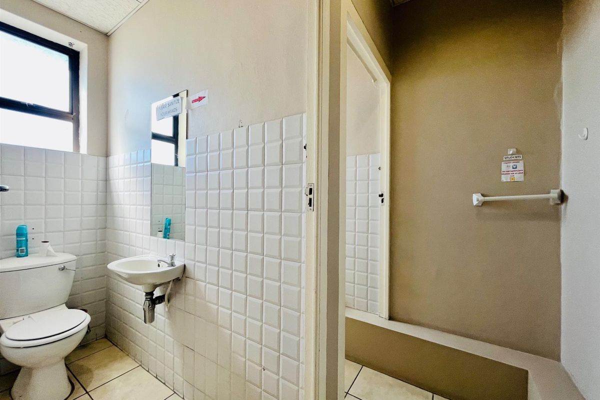 A functional commercial bathroom featuring a wall-mounted basin, toilet, and tiled finishes, requiring cosmetic updates to improve its overall condition.