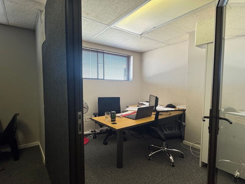 A functional commercial office space featuring carpeted flooring, a suspended ceiling with integrated lighting, and a glass partition entrance.