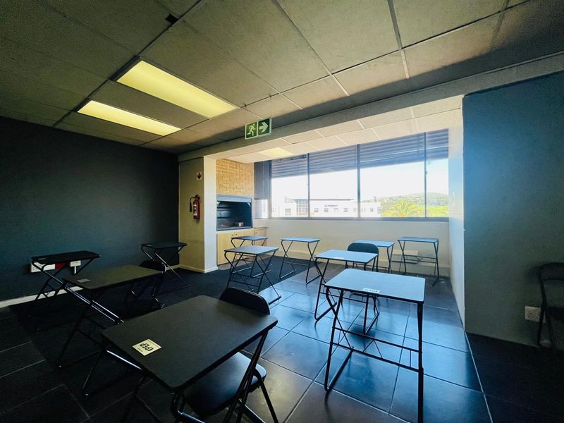 Commercial office space featuring tiled flooring, suspended ceiling with recessed lighting, large windows, and a built-in braai area.