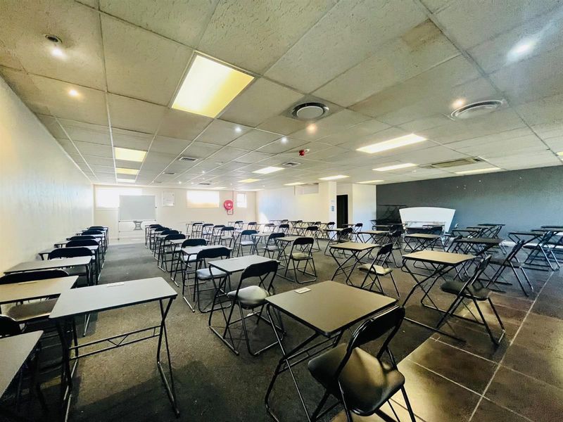 A large commercial office or training space featuring a suspended ceiling, recessed lighting, and tiled flooring, currently set up with multiple desks.
