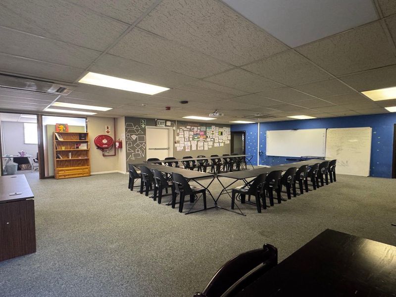 Spacious commercial office or training room featuring carpeted flooring, suspended ceilings, integrated lighting, and wall-mounted whiteboards, suitable for professional meetings or educational use.