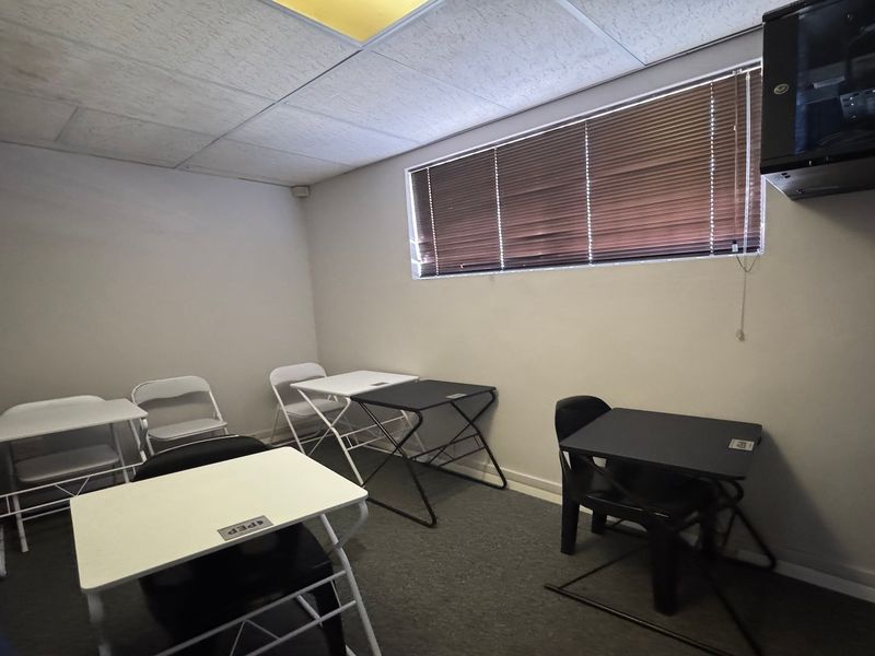 A functional office space featuring carpeted flooring, a suspended ceiling, and a wall-mounted server cabinet, suitable for a small commercial workspace.