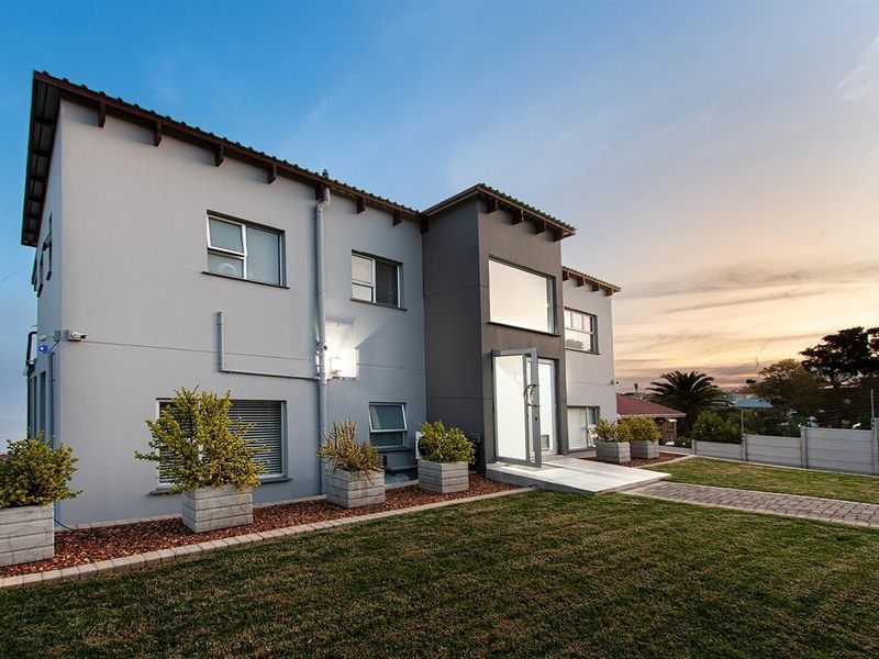 A modern two-story residential building exterior featuring a paved walkway, landscaped garden area, and contemporary architectural design with large windows.