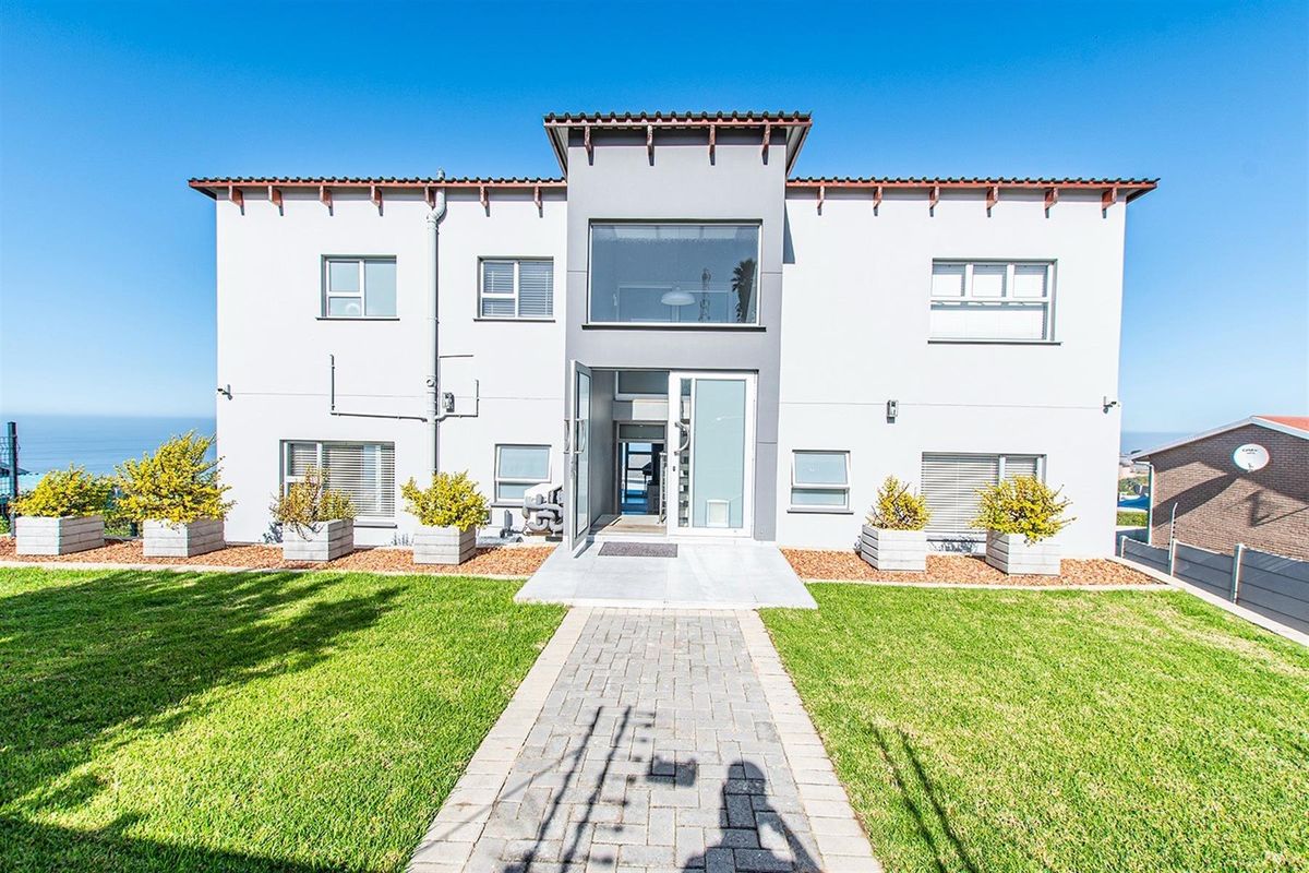 Front exterior view of a modern apartment building featuring a paved walkway, manicured lawn, and a central entrance with large glass windows.