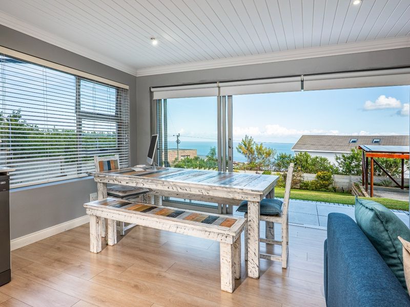 Bright open plan living area featuring wood-look flooring, recessed ceiling lighting, and large sliding glass doors opening to a patio with scenic ocean views.