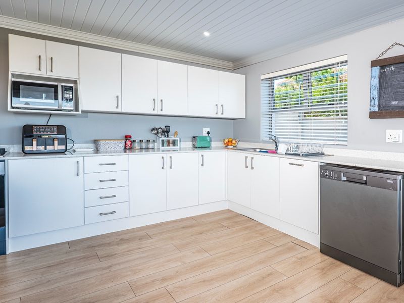 Modern kitchen featuring white cabinetry, stone-look countertops, integrated oven, and wood-look flooring, offering a clean and functional workspace.