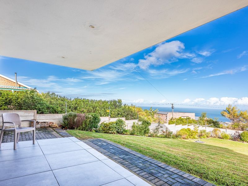 A covered patio area featuring tiled flooring, overlooking a landscaped garden with expansive coastal and ocean views.