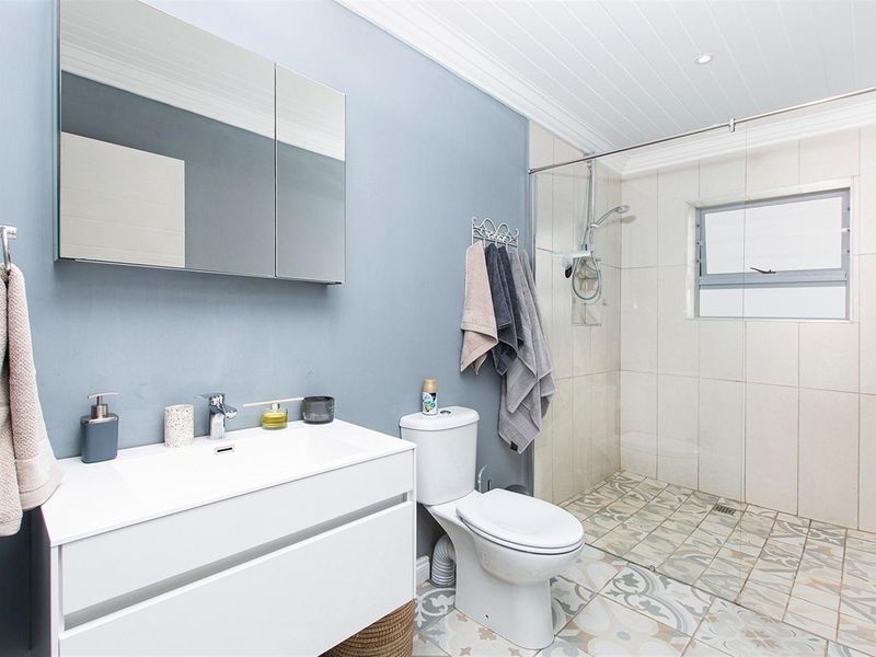 Modern bathroom featuring a walk-in shower with glass screen, vanity unit with integrated basin, mirrored cabinet, and patterned floor tiling.