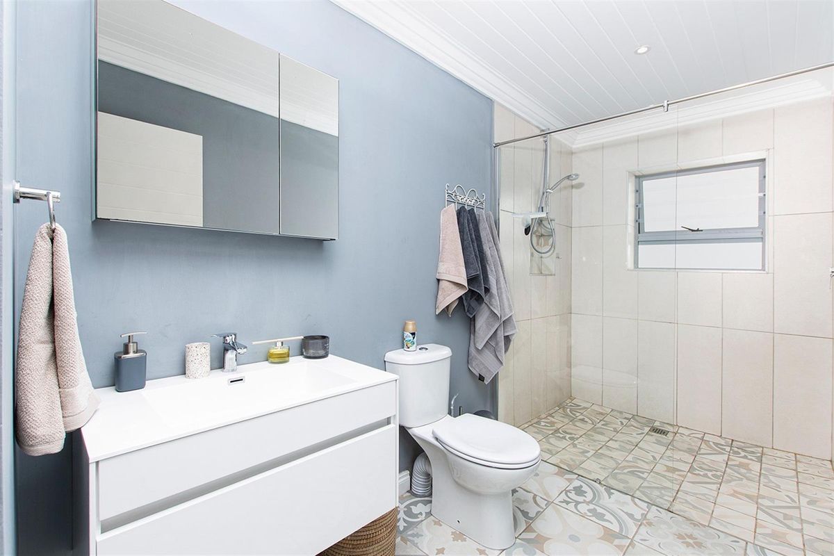 Modern bathroom featuring a walk-in shower with glass screen, vanity unit with integrated basin, mirrored cabinet, and patterned floor tiling.