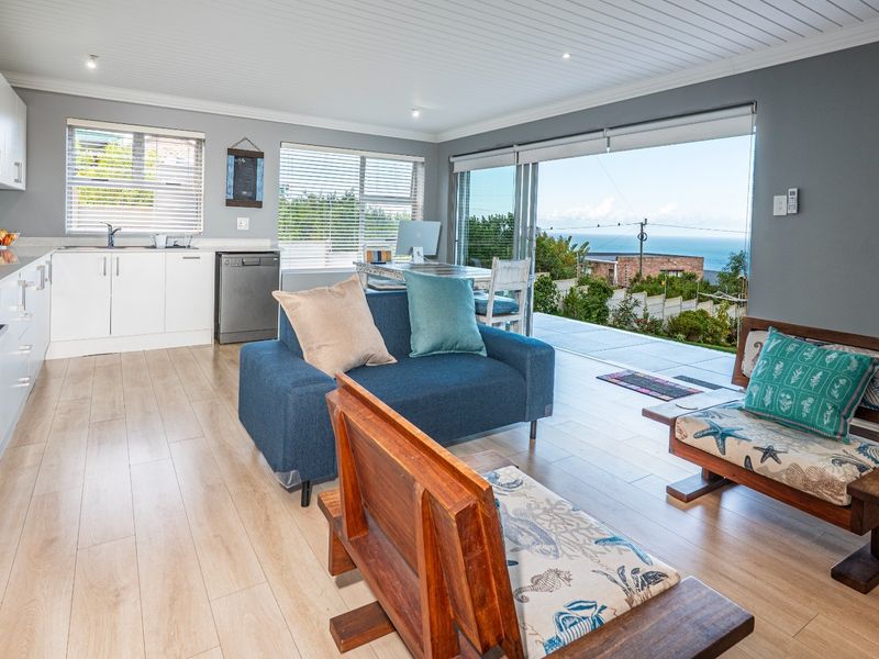 Open-plan living area featuring a modern kitchen with white cabinetry, light wood-look flooring, and large sliding doors opening to a scenic coastal view.