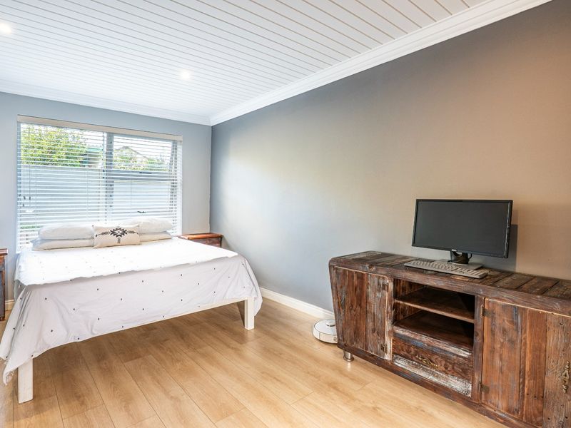 A well-maintained bedroom featuring light wood-look flooring, a unique tongue-and-groove ceiling, and a large window with fitted blinds.