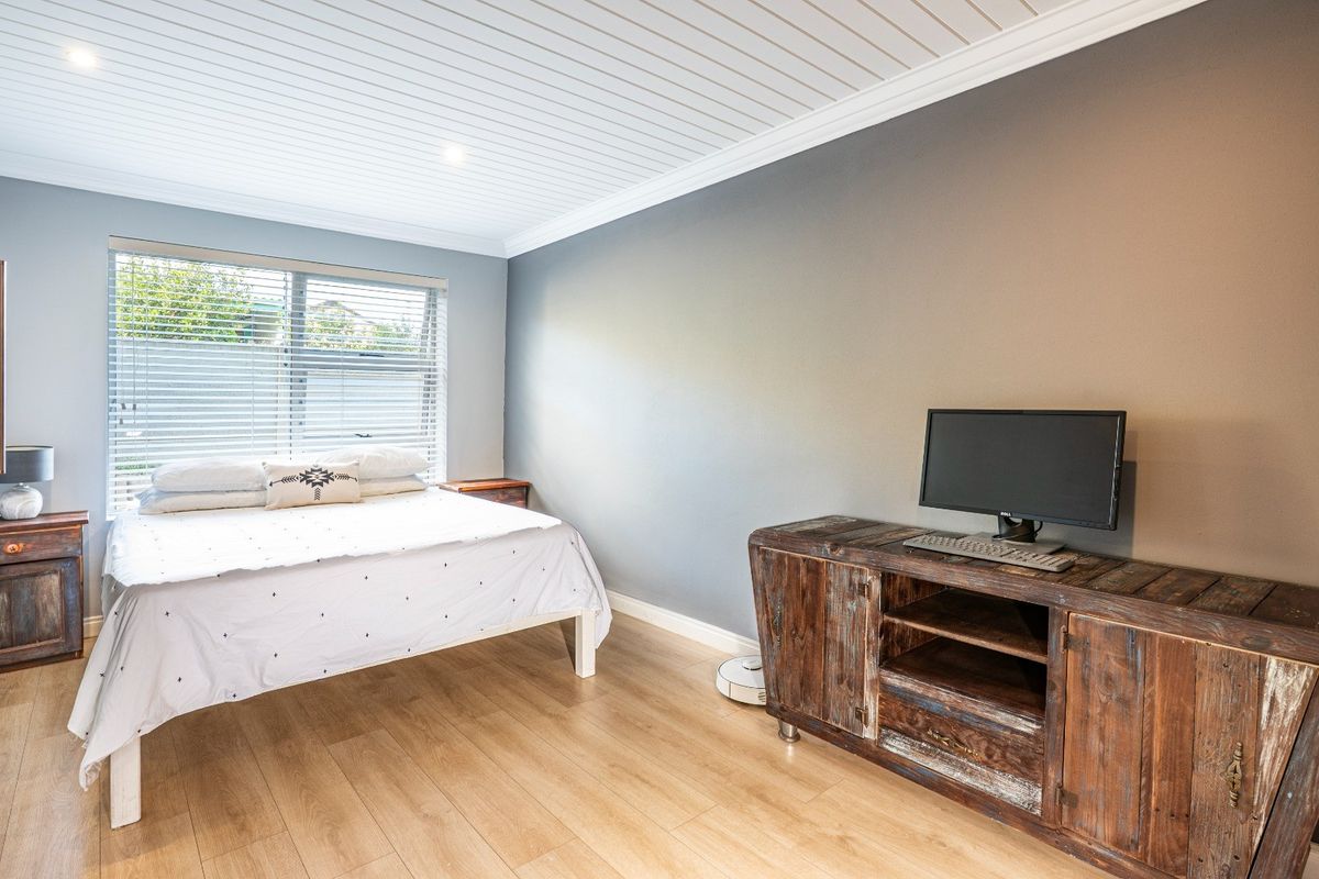 A well-maintained bedroom featuring light wood-look flooring, a unique tongue-and-groove ceiling, and a large window with fitted blinds.