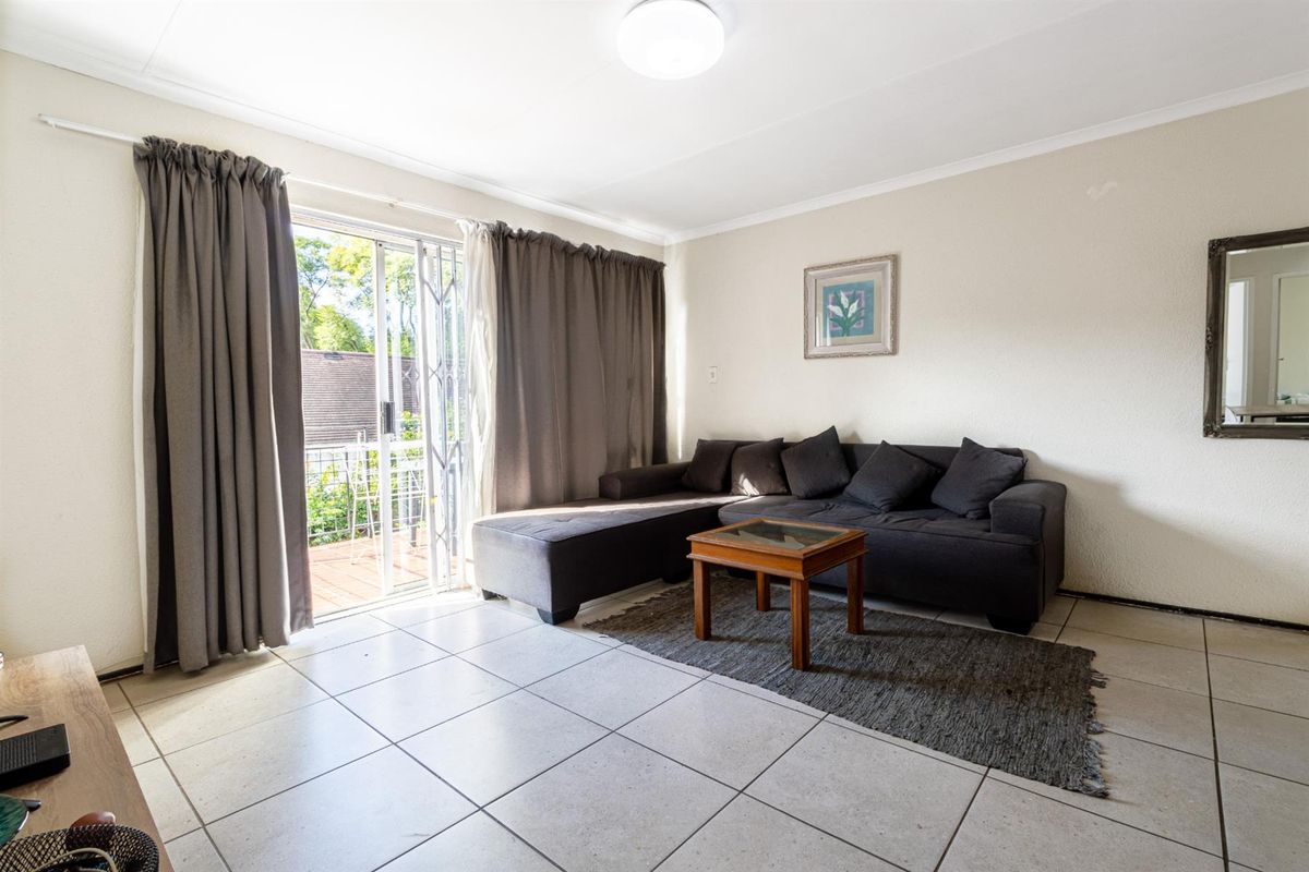 A bright living room featuring neutral tiled flooring and a sliding glass door providing access to an outdoor balcony area.
