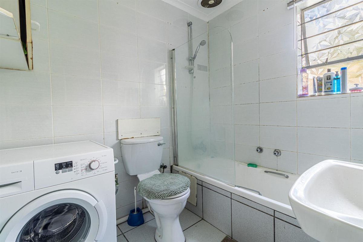 A functional bathroom featuring a bathtub with a glass screen, pedestal basin, and toilet, with integrated laundry space and tiled finishes throughout.