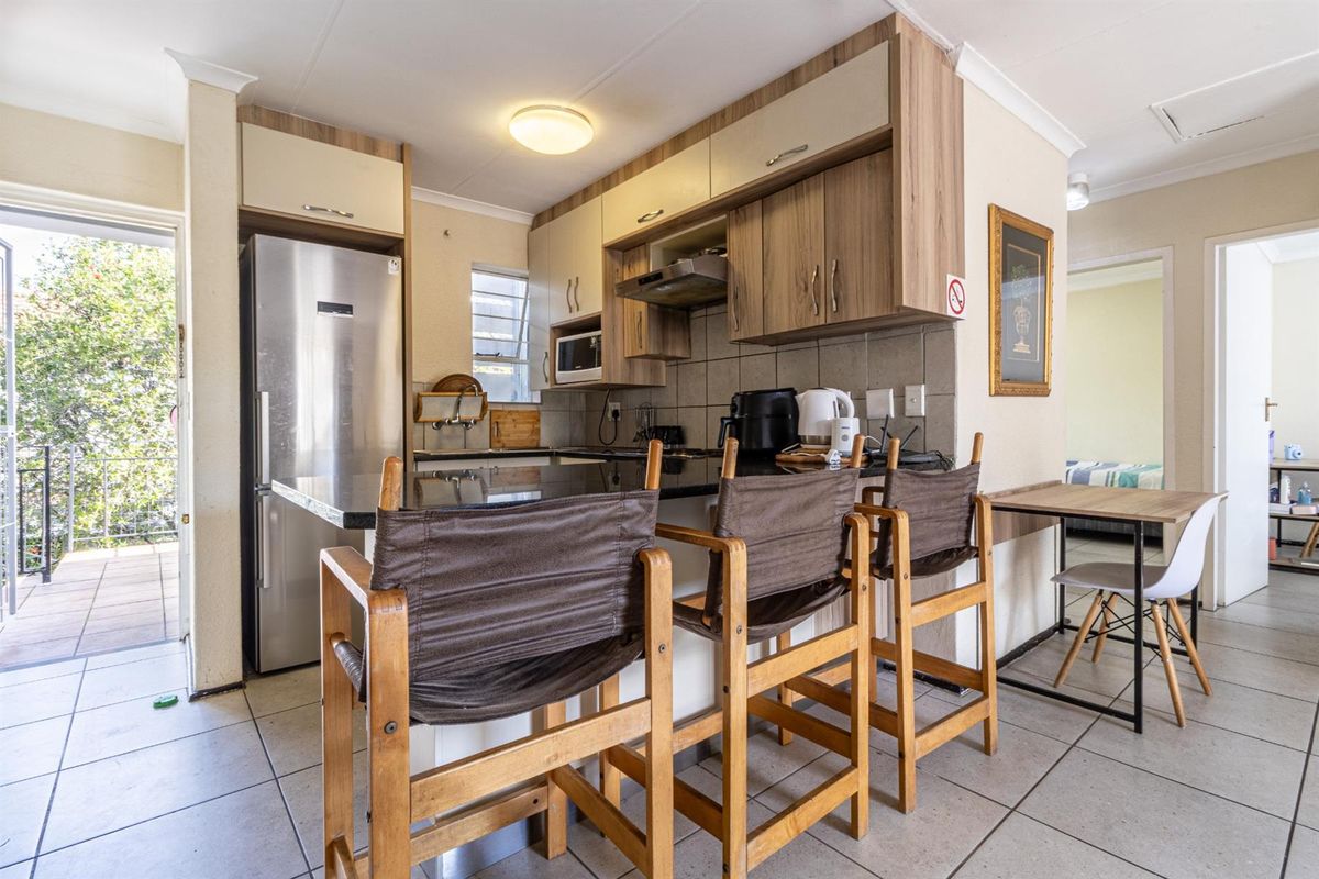 Compact kitchen featuring wood-finish cabinetry, granite countertops, tiled backsplash, and an integrated extractor fan, with direct access to an outdoor balcony area.