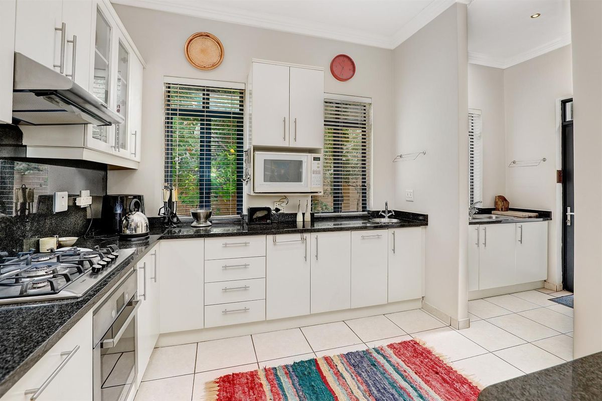 A well-maintained kitchen featuring white cabinetry, dark granite countertops, a built-in gas hob, oven, and an adjacent scullery area with additional sink and storage.