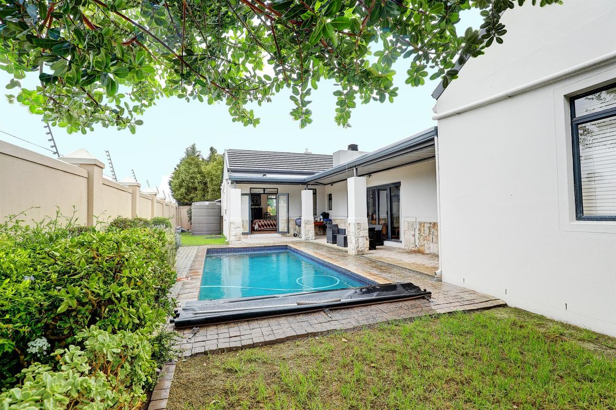 Rear exterior view featuring a swimming pool, paved patio area, and well-maintained garden with perimeter walling.
