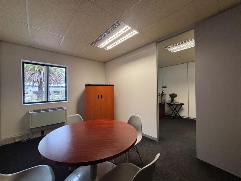 A functional office space featuring carpeted flooring, recessed fluorescent lighting, and an integrated HVAC unit, with an adjacent room visible through a sliding door.
