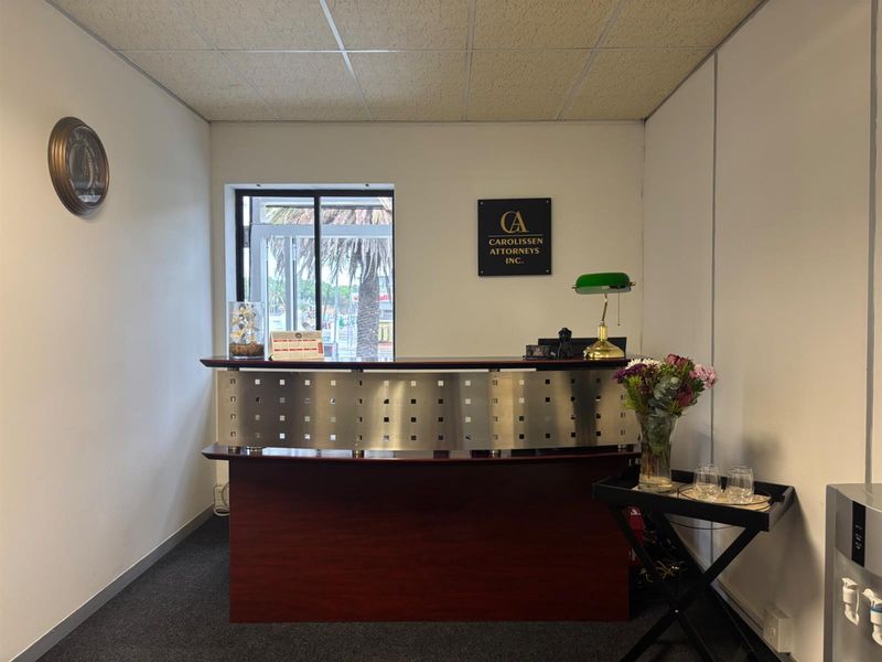 A professional office reception area featuring a built-in reception desk, suspended ceiling tiles, and natural light from a side window.