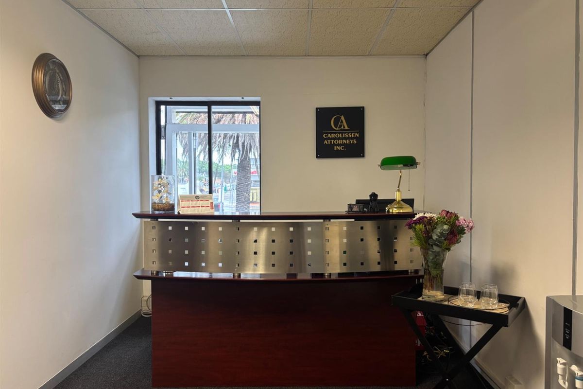 A professional office reception area featuring a built-in reception desk, suspended ceiling tiles, and natural light from a side window.