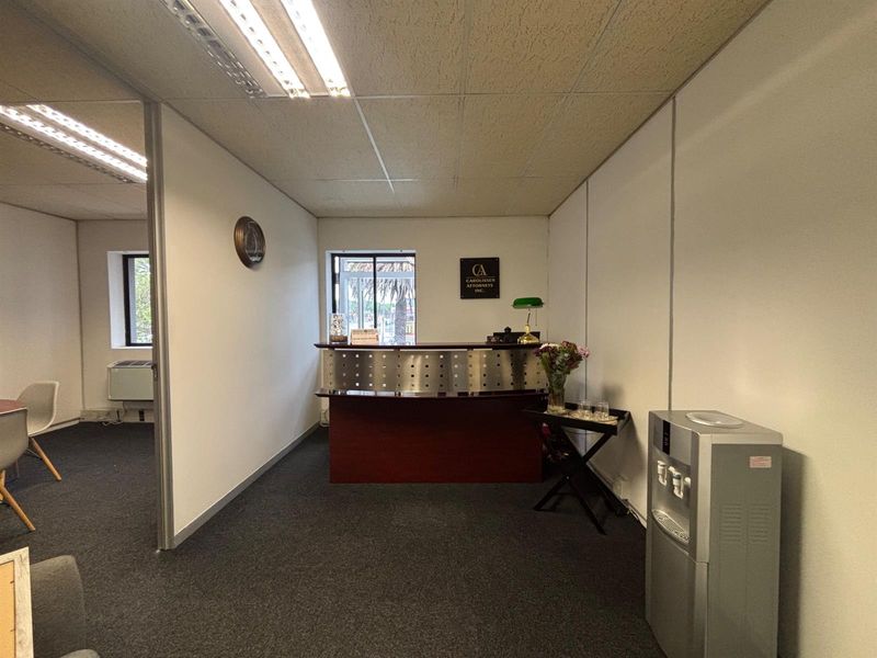 Professional office reception area featuring a built-in reception desk, suspended ceiling, and carpeted flooring, providing a functional workspace for clients and staff.