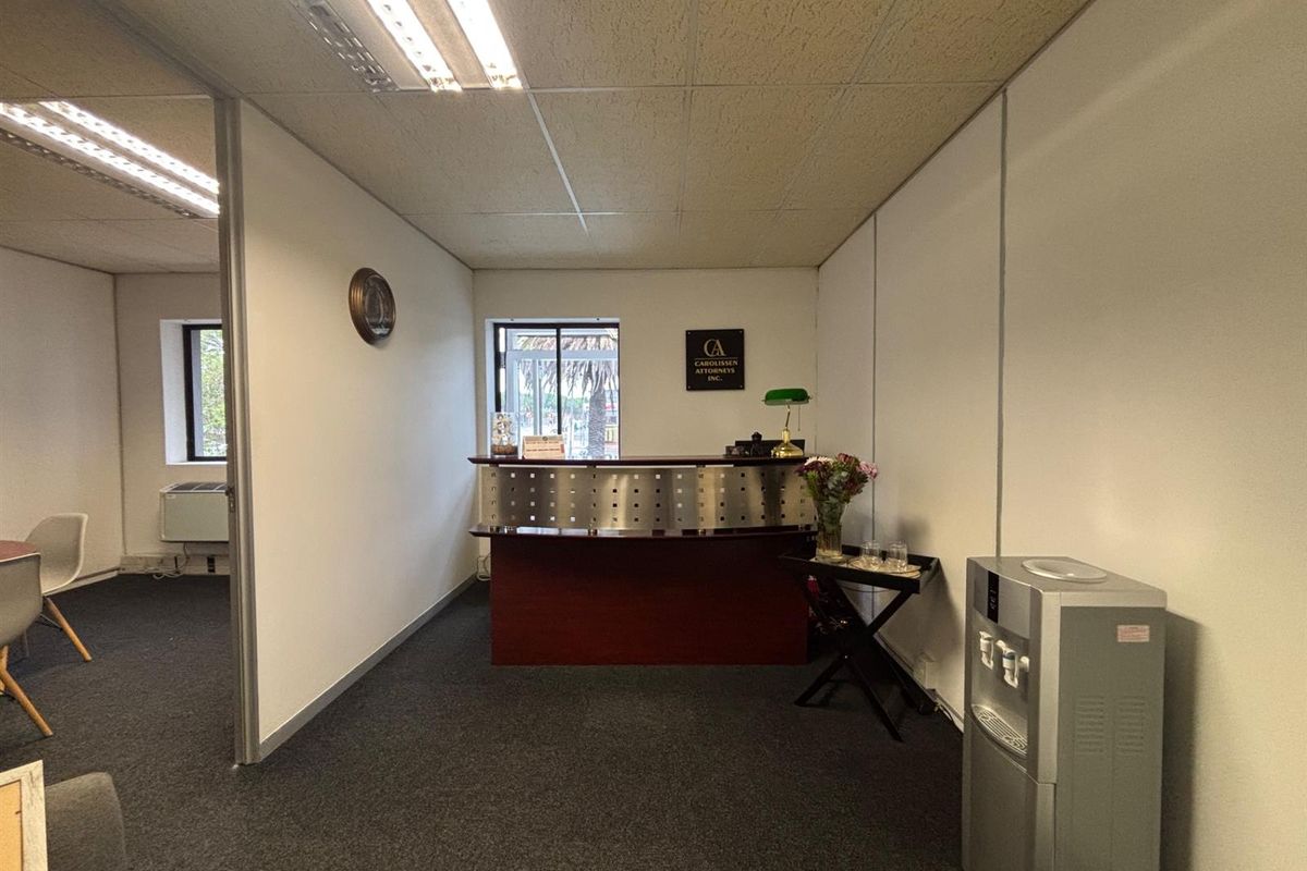 Professional office reception area featuring a built-in reception desk, suspended ceiling, and carpeted flooring, providing a functional workspace for clients and staff.