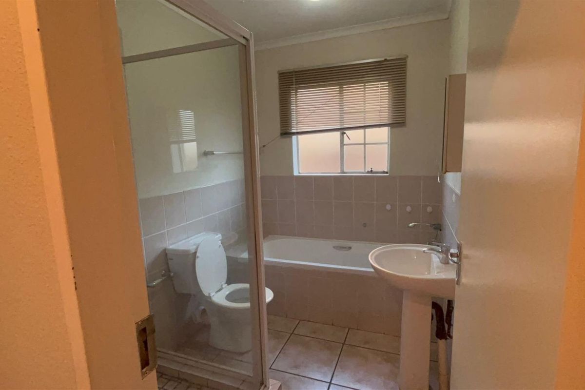 A functional bathroom featuring a pedestal basin, bathtub, and a separate shower enclosure with tiled finishes and neutral wall tones.