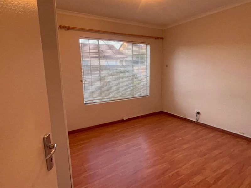 An empty bedroom featuring laminate flooring, neutral walls, and a window fitted with venetian blinds and a curtain rod.