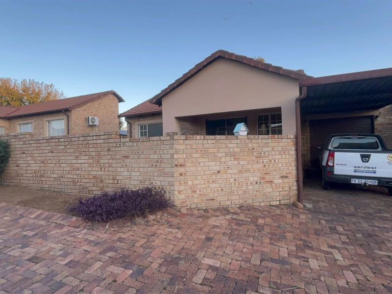 Front view of a townhouse featuring a face brick boundary wall, paved driveway, and a covered carport area.