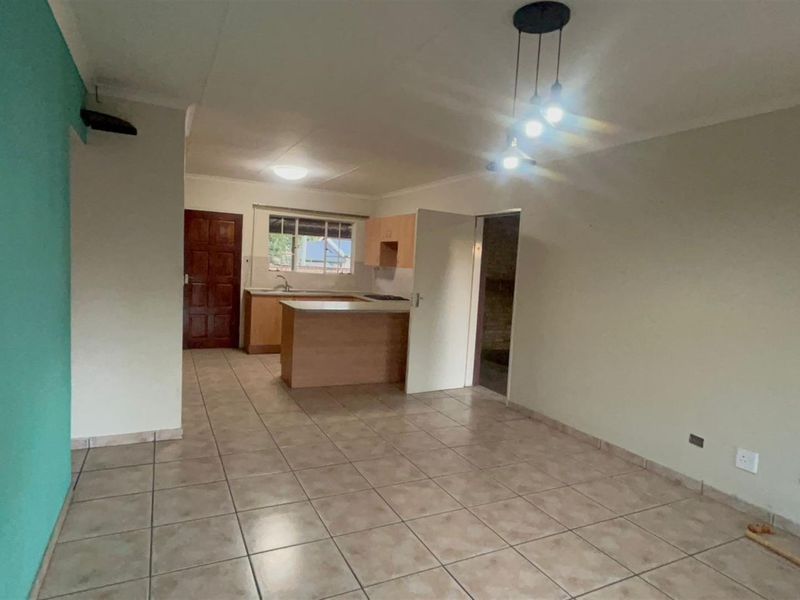 An open-plan living and kitchen area featuring tiled flooring, neutral wall tones, and functional kitchen cabinetry, offering a blank canvas for personalization.