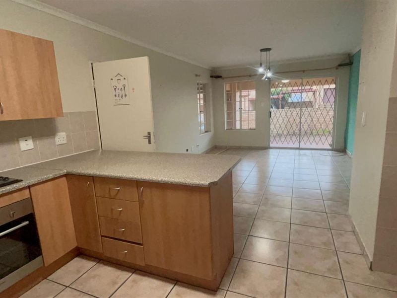 Open-plan kitchen and living area featuring tiled flooring, wooden cabinetry, built-in oven, and a sliding door leading to the exterior.