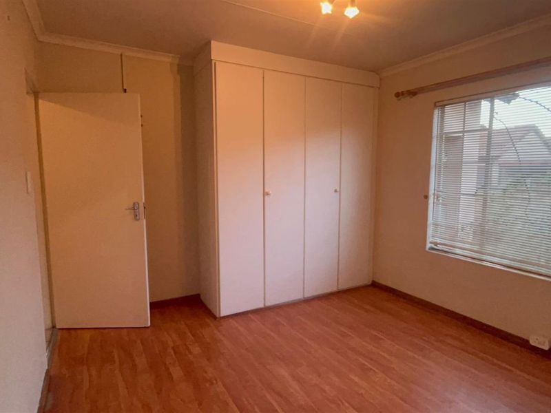 A vacant bedroom featuring laminate flooring, built-in cupboards, and venetian blinds, offering a neutral canvas for personalization.