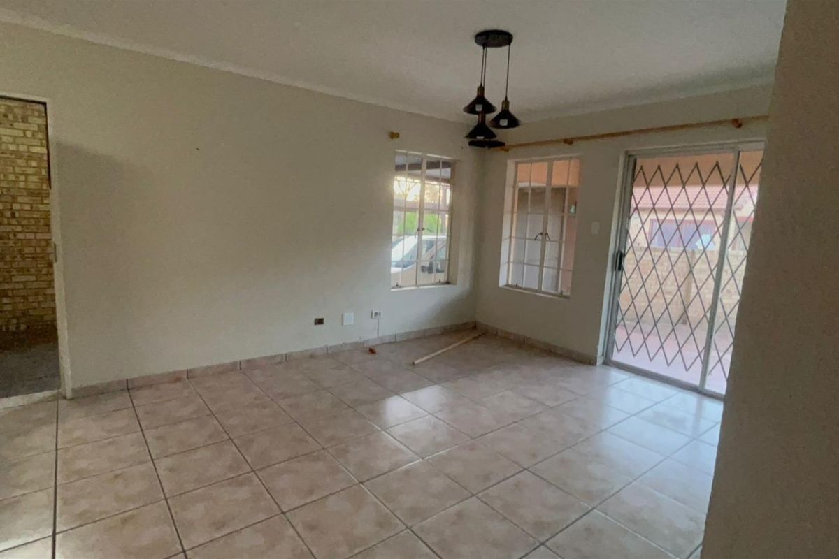 An empty living room featuring tiled flooring, pendant lighting, and a sliding glass door with a security gate leading to the exterior.