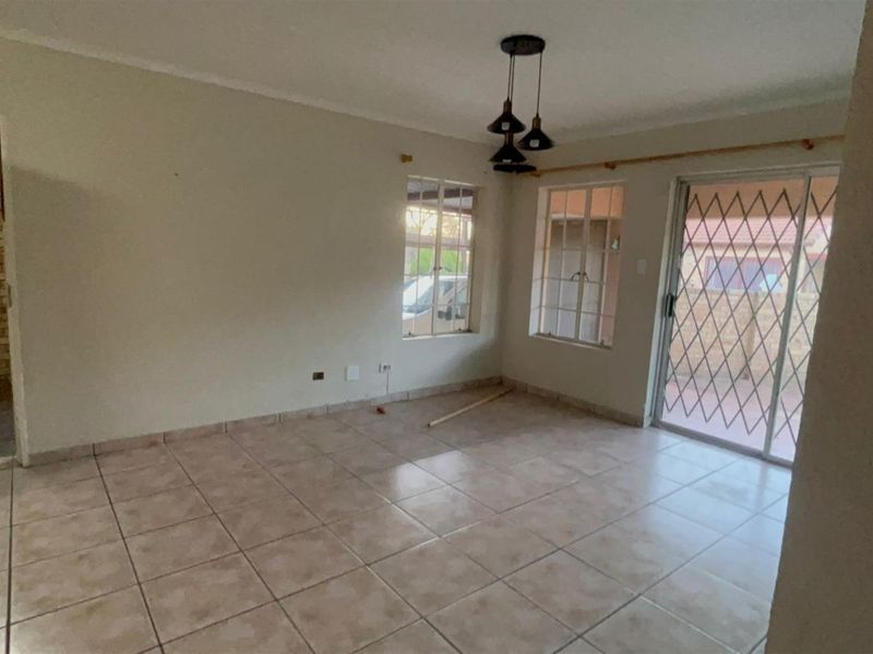 An empty living room featuring tiled flooring, pendant lighting, and a sliding glass door with a security gate leading to the exterior.