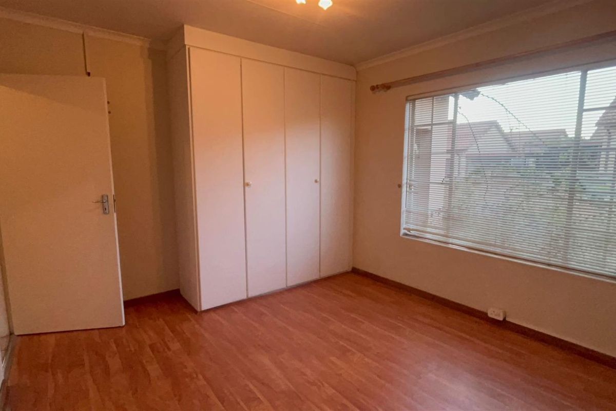 A vacant bedroom featuring laminate flooring, built-in cupboards, and window blinds, offering a clean and neutral space ready for personalization.