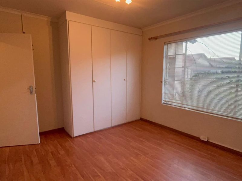 A vacant bedroom featuring laminate flooring, built-in cupboards, and window blinds, offering a clean and neutral space ready for personalization.