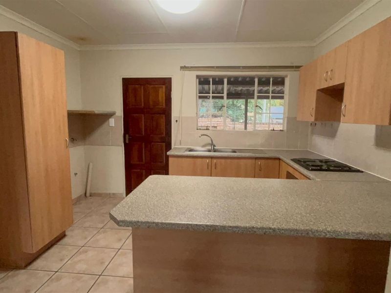 A functional kitchen featuring laminate cabinetry, stone-look countertops, a built-in gas hob, and tiled flooring, offering a blank canvas for potential updates.